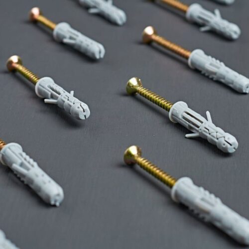 Rows of many new plastic gray dowel with glossy screw golden color for repair and fixing different predmet on wall lies on scratches dark concrete table in workshop. Close-up